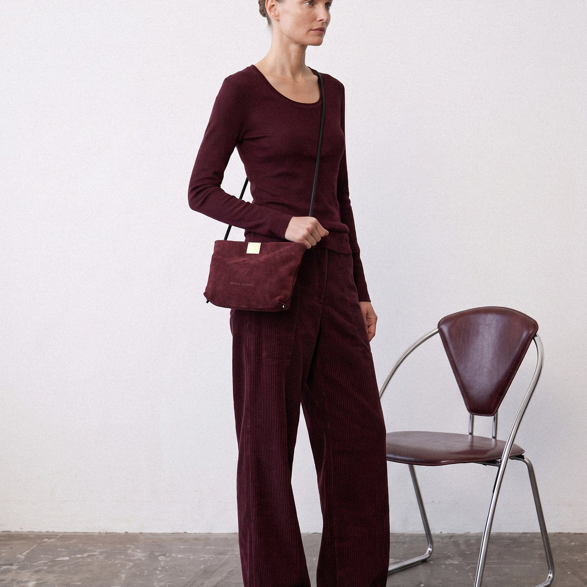Woman in a tonal wine-red outfit wearing the Capri Clutch in Bordeaux, a Bordeaux suede bag