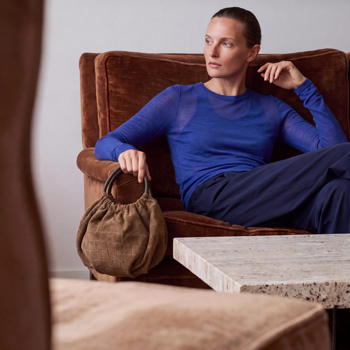 Model seated on a velvet sofa with the Salina Wristlet in Brown Croco suede
