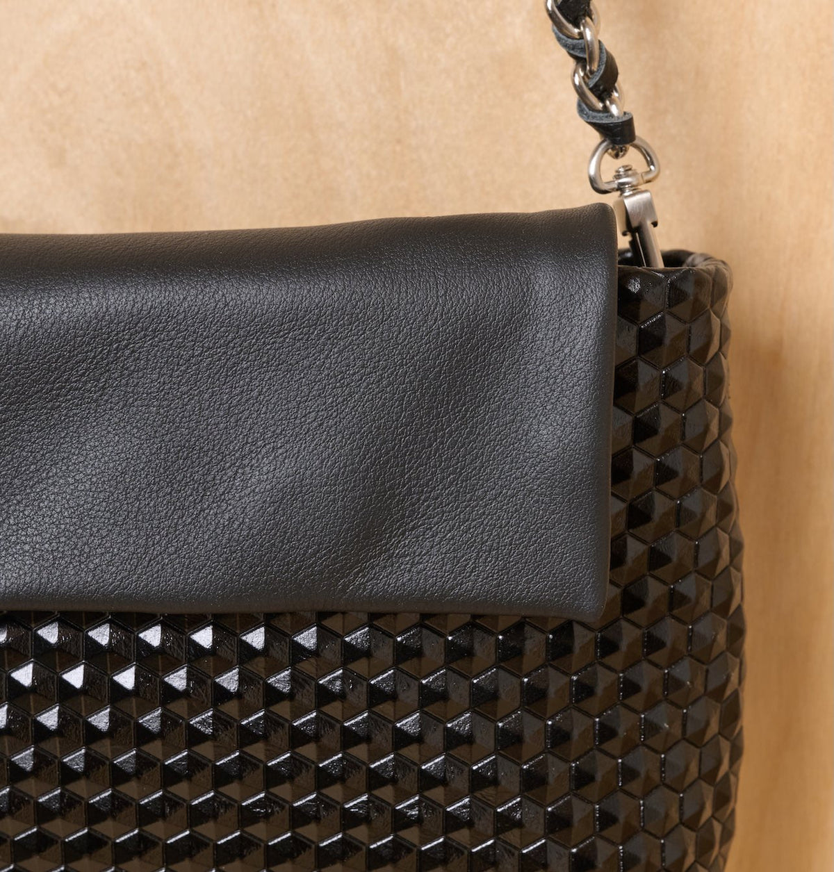 תיק שחור עם דש עור מחוספס וגוף בדוגמת דפוס גיאומטרי תלת-מימדי של יהלומים, ורצועת שרשרת.