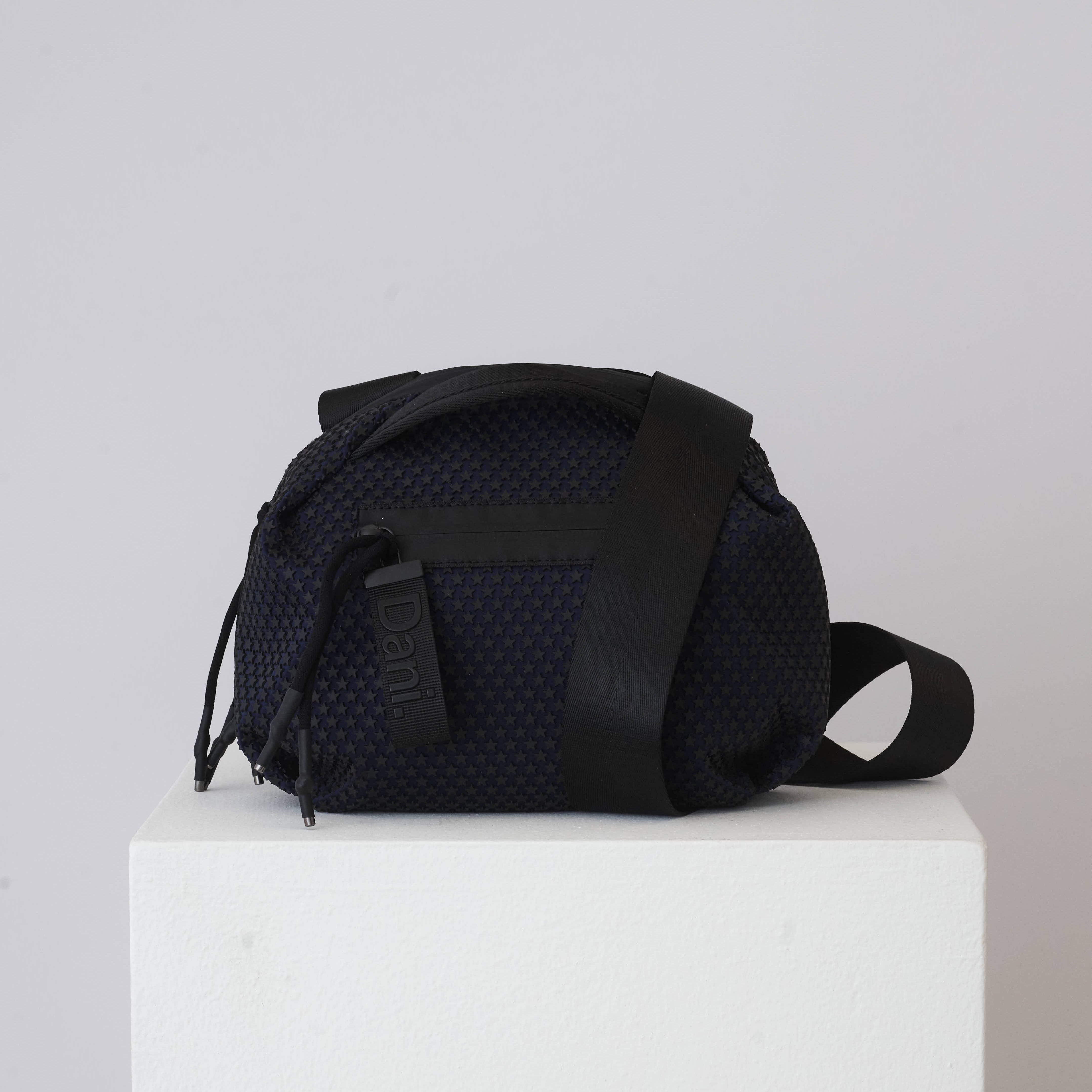 Black textured bag on a white pedestal with a light gray background