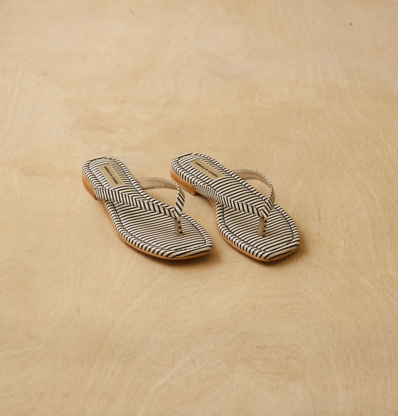 שני כפכפים בדוגמת פסים בשחור-לבן עם רצועת אצבע בהירה, על רקע עץ בהיר.