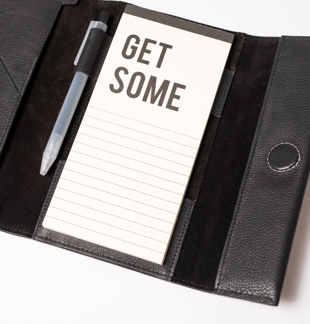 מארגן עור שחור פתוח, עם פנקס 'GET SOME', עט שקוף וכפתור סגירה.