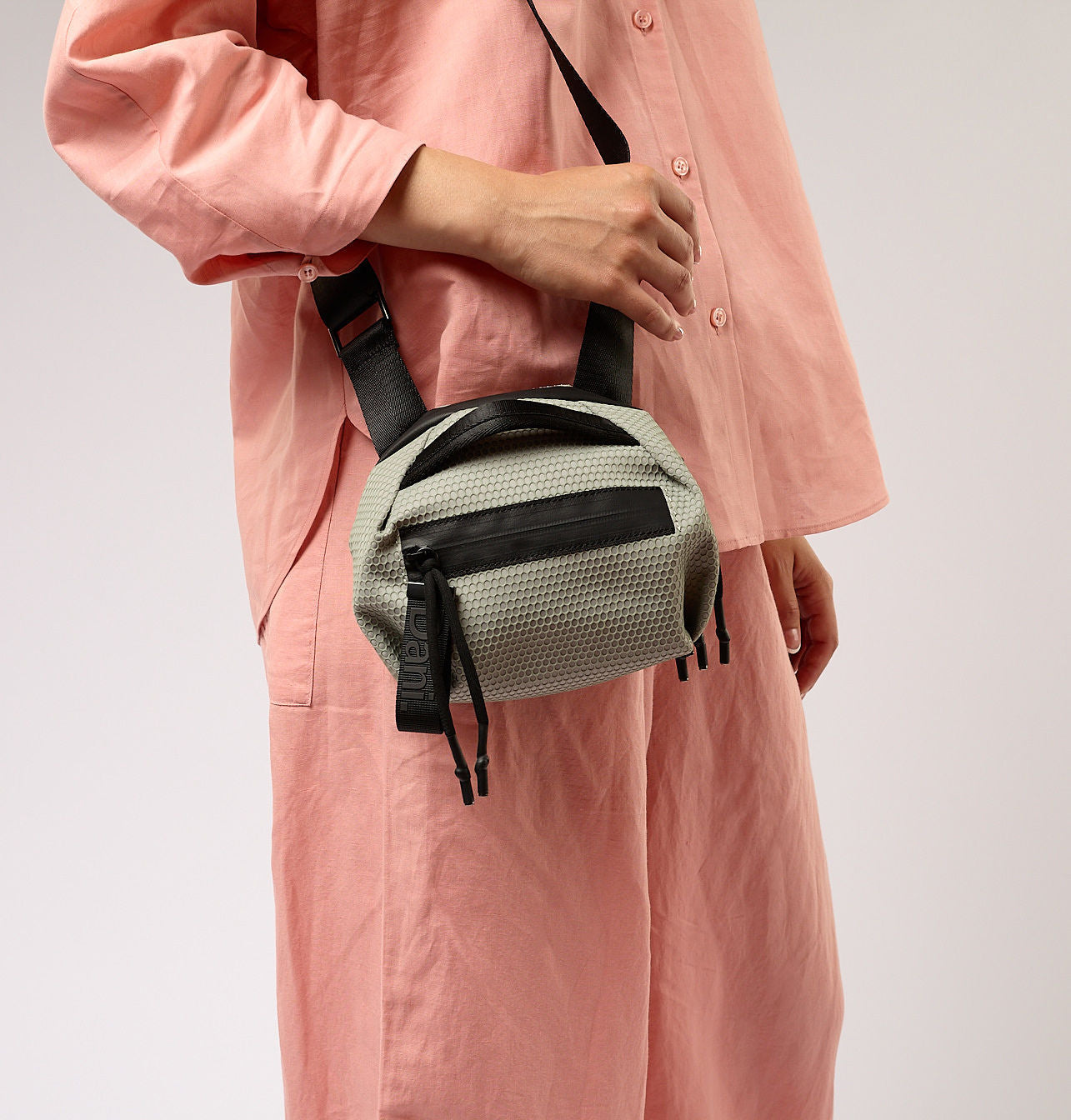 Person wearing a pink outfit with a beige and black bag on a plain background