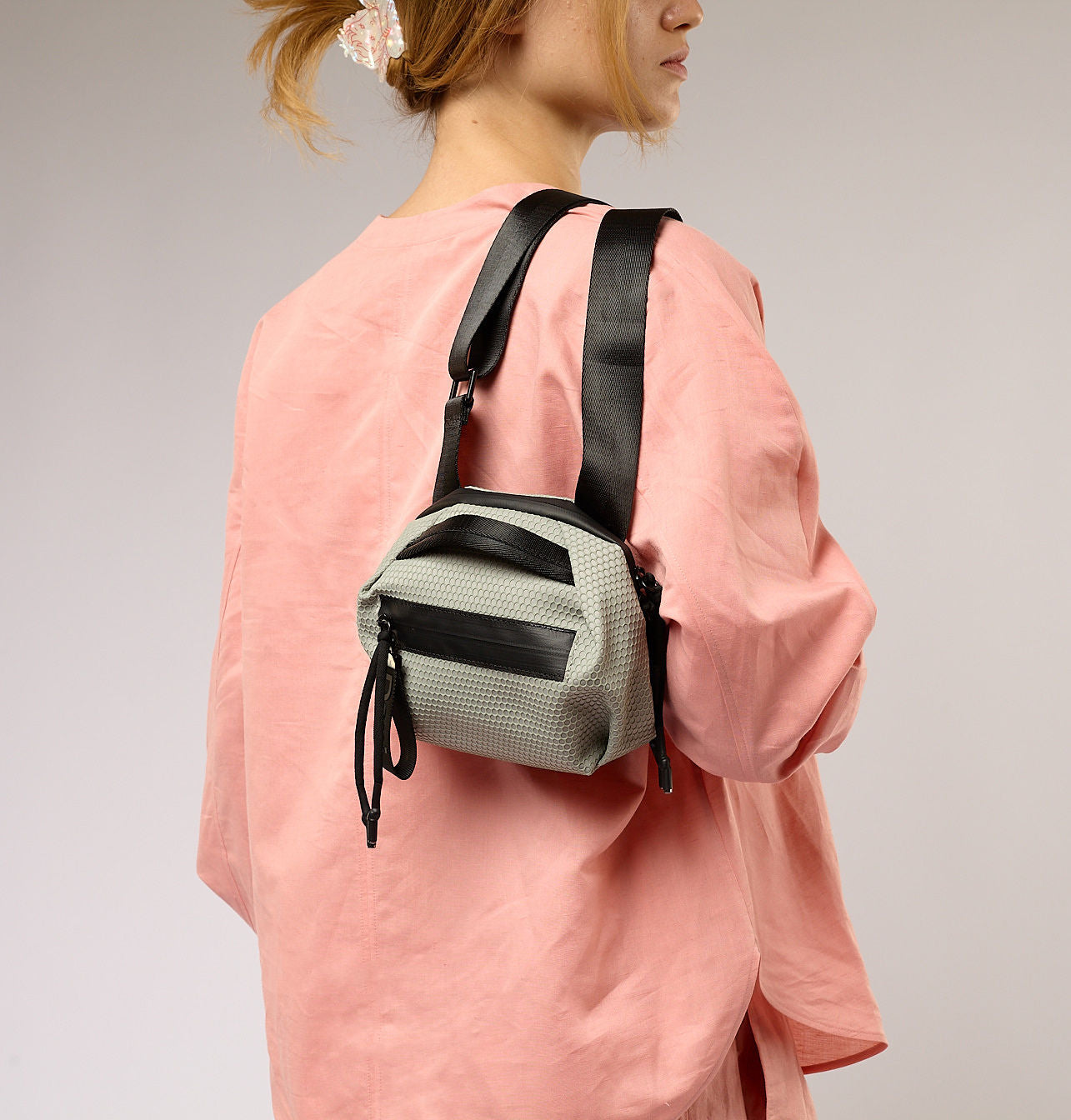 Person wearing a small green backpack with black straps on a plain background