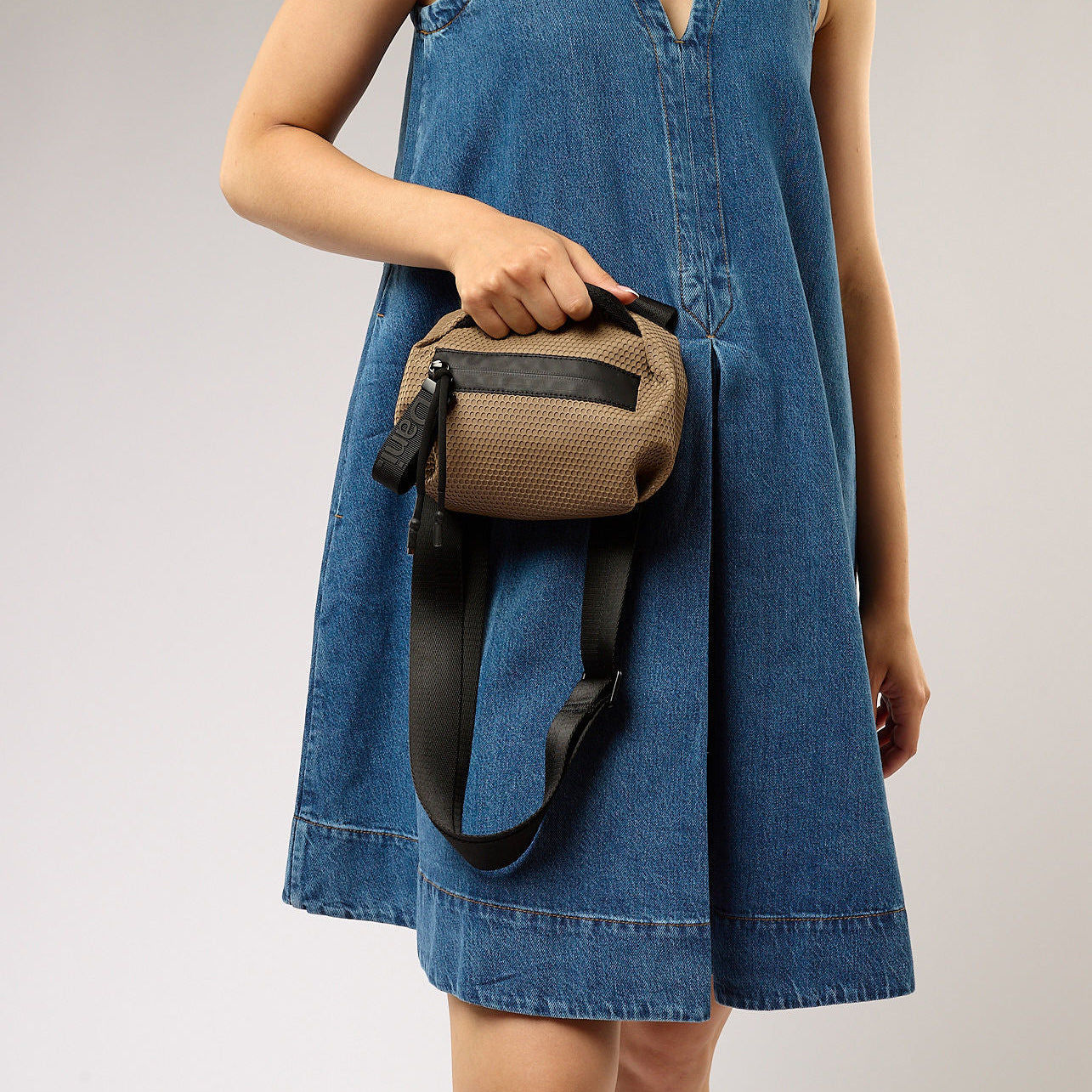 Person wearing a blue dress holding a brown bag with a black strap on a plain background