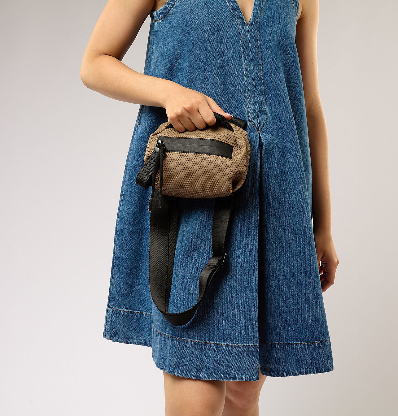 Person wearing a blue dress holding a brown bag with a black strap on a plain background