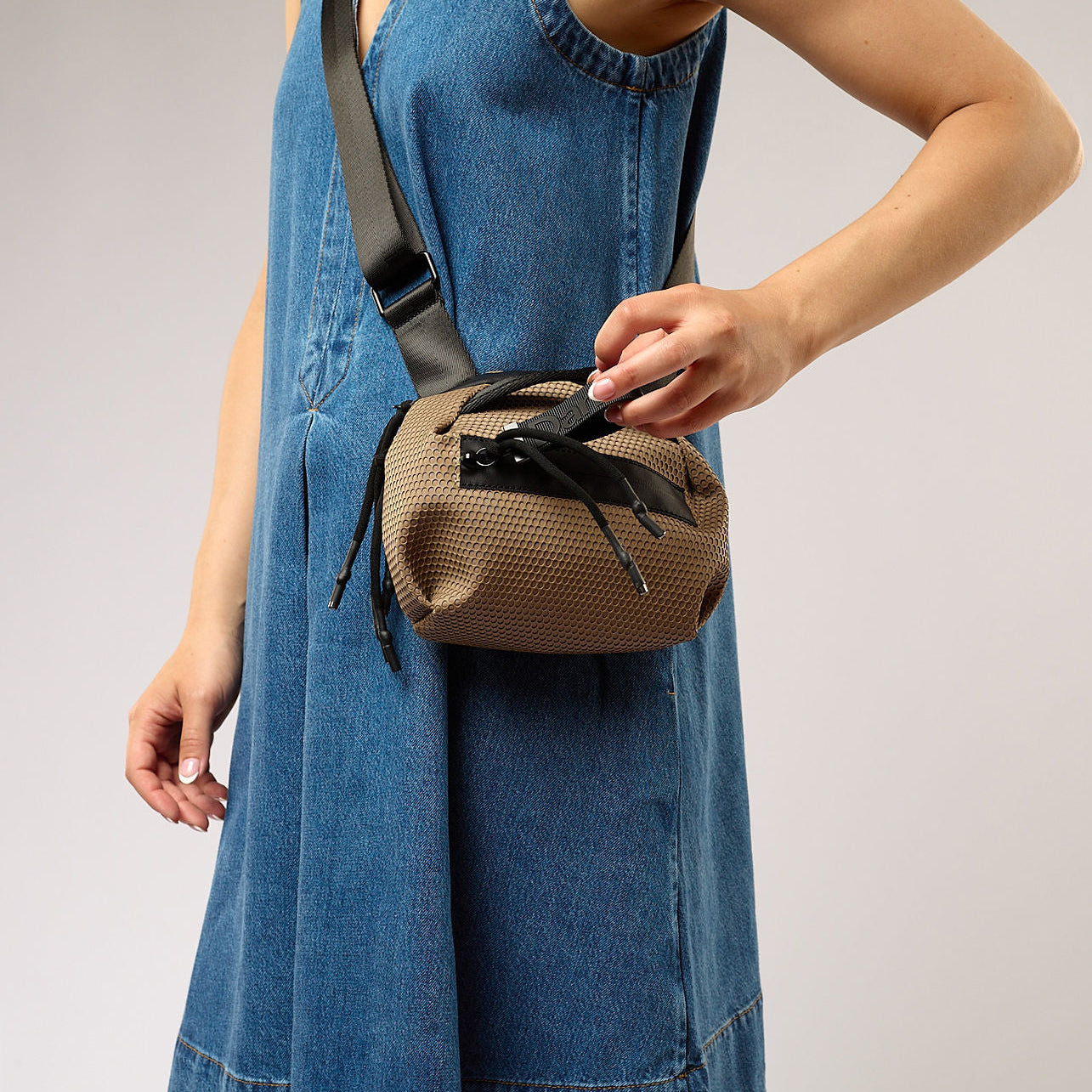 Person wearing a denim dress with a brown woven bag over their shoulder on a plain background