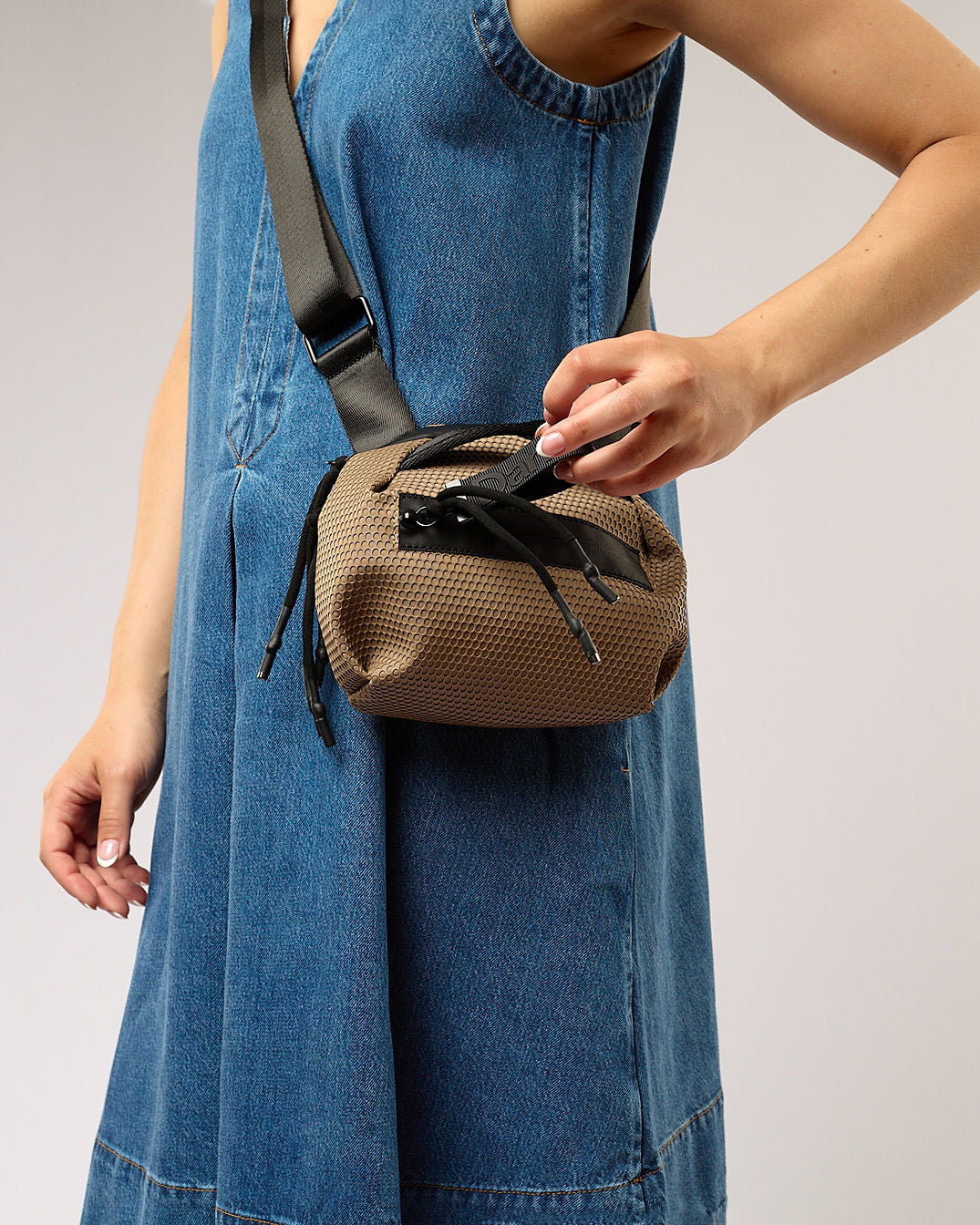 Person wearing a denim dress with a brown woven bag over their shoulder on a plain background