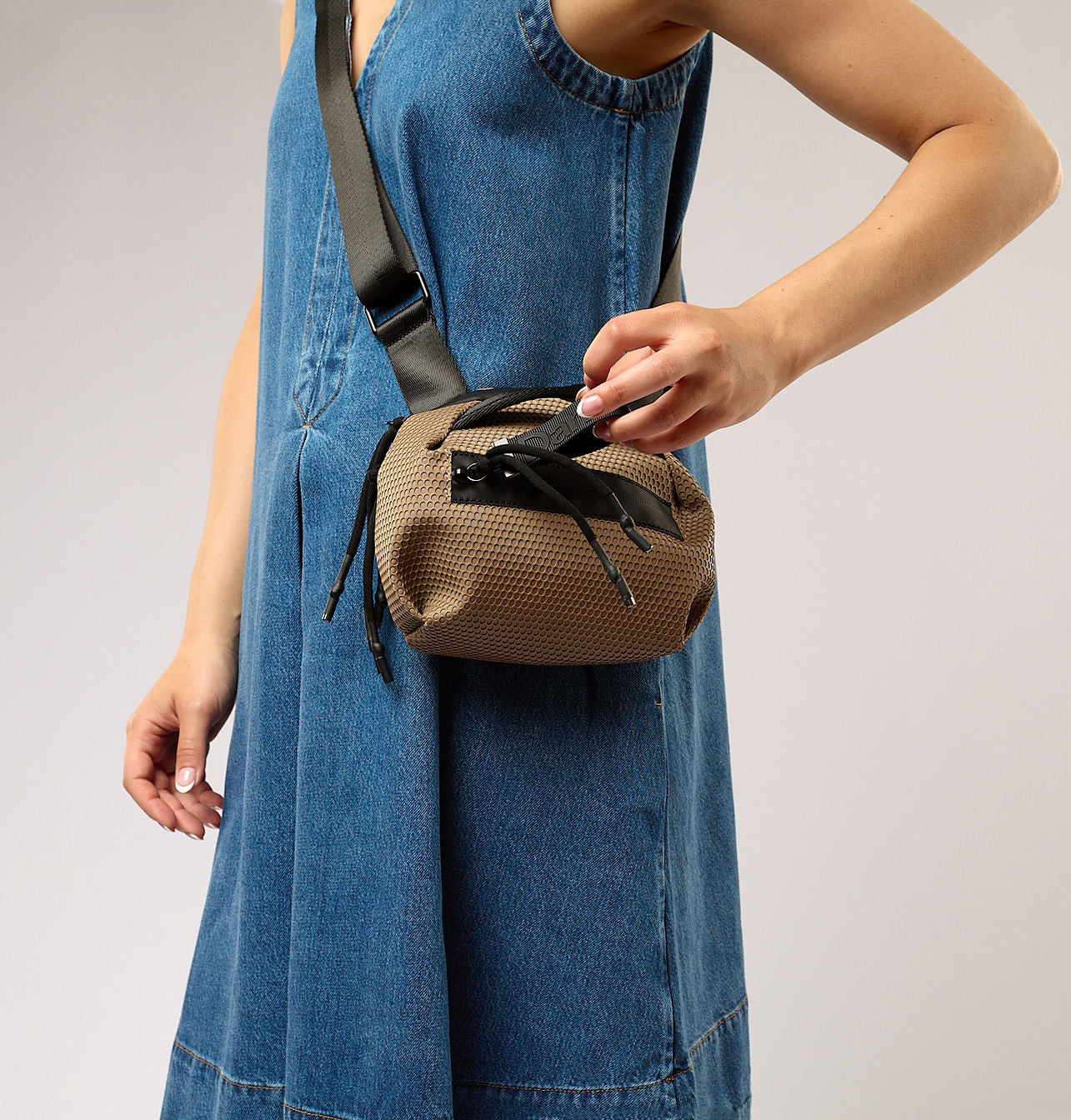 Person wearing a denim dress with a brown woven bag over their shoulder on a plain background
