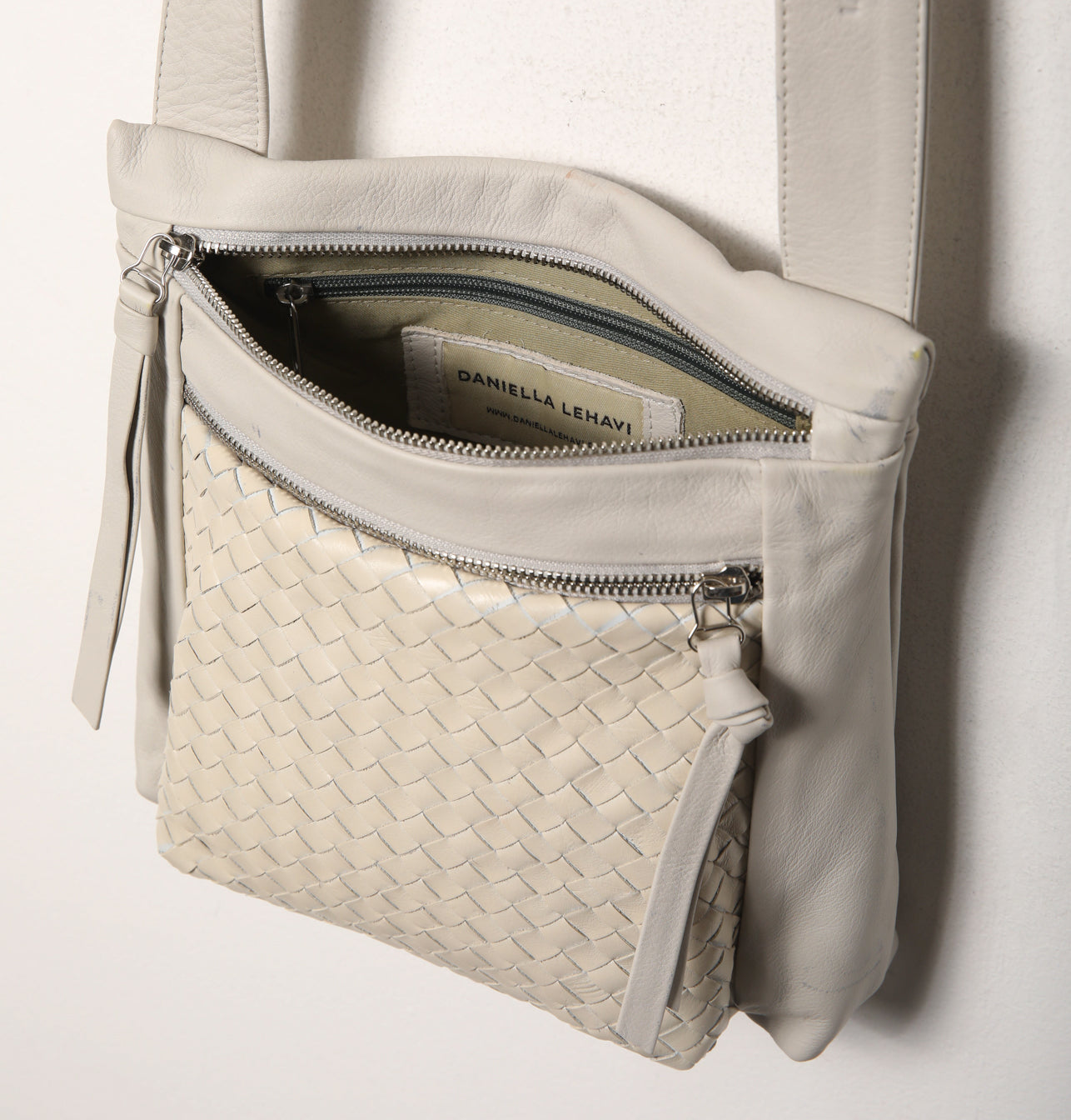 תיק צד בצבע קרם פתוח עם שני רוכסנים, כיס קדמי קלוע ורצועת כתף.