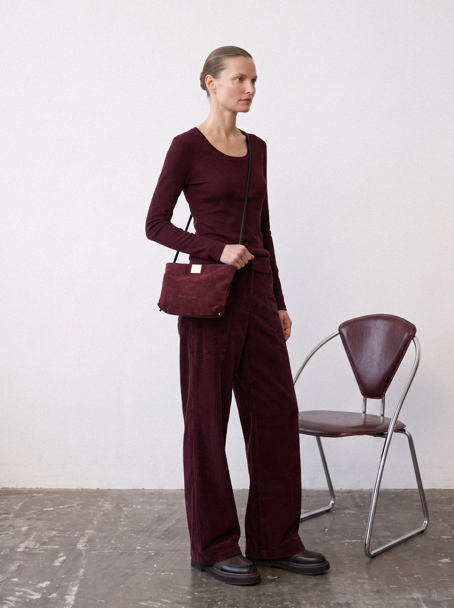 Woman in a tonal wine-red outfit wearing the Capri Clutch in Bordeaux, a Bordeaux suede bag
