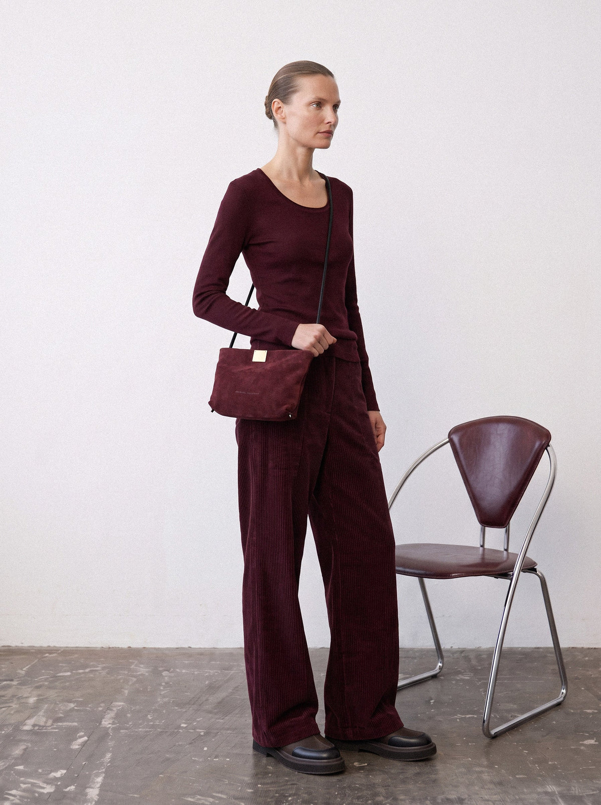 Woman in a tonal wine-red outfit wearing the Capri Clutch in Bordeaux, a Bordeaux suede bag