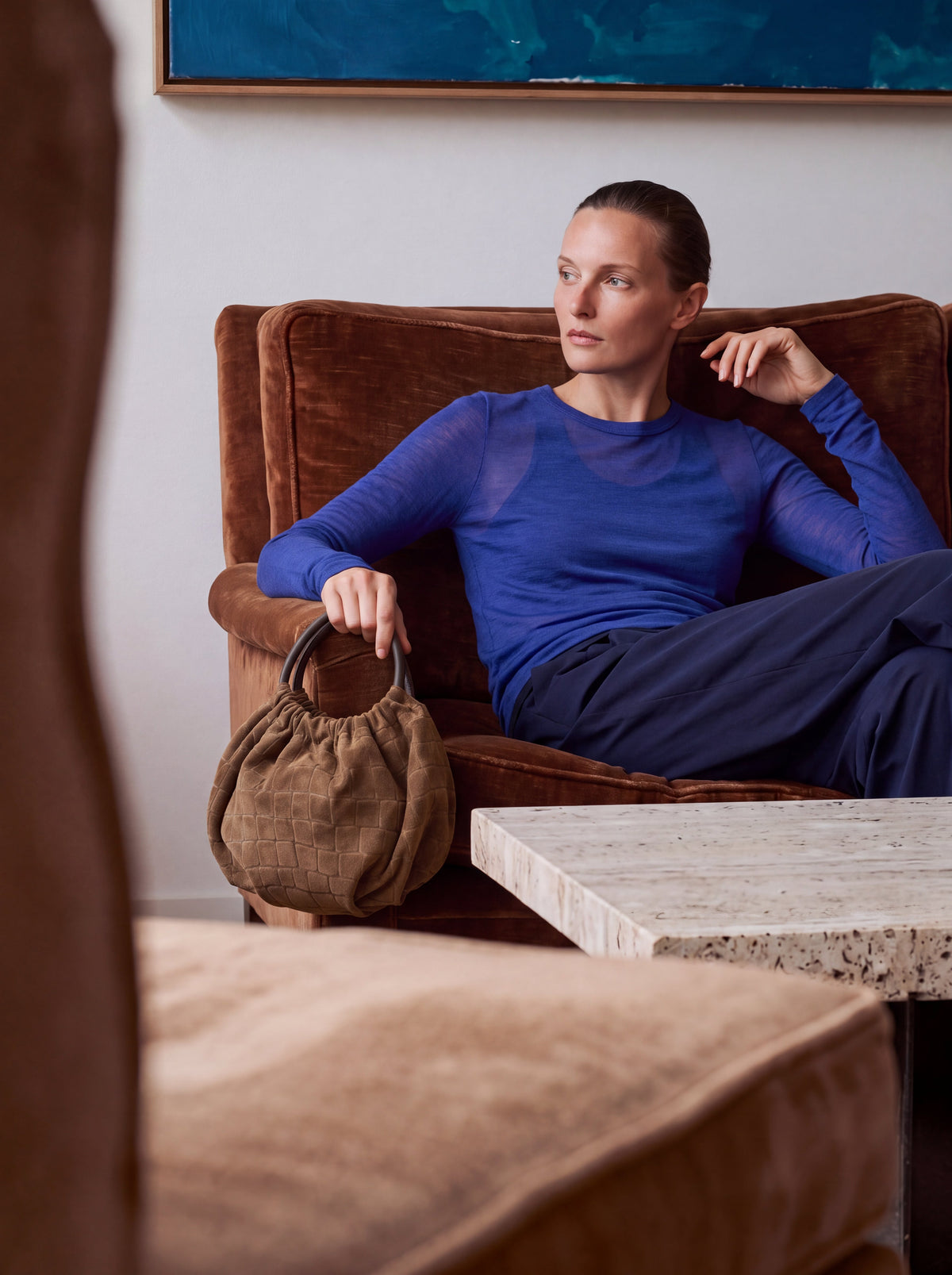 Model seated on a velvet sofa with the Salina Wristlet in Brown Croco suede