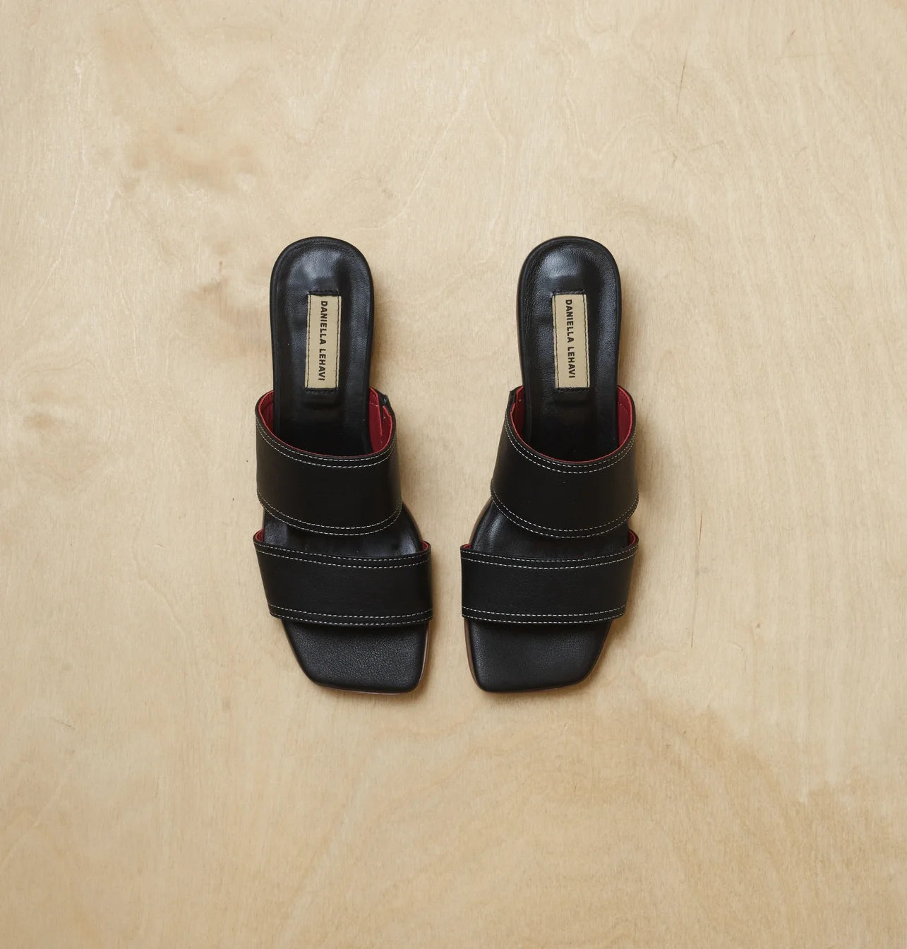 זוג כפכפים שחורים עם רצועות רחבות ותפירה לבנה על רקע בהיר.