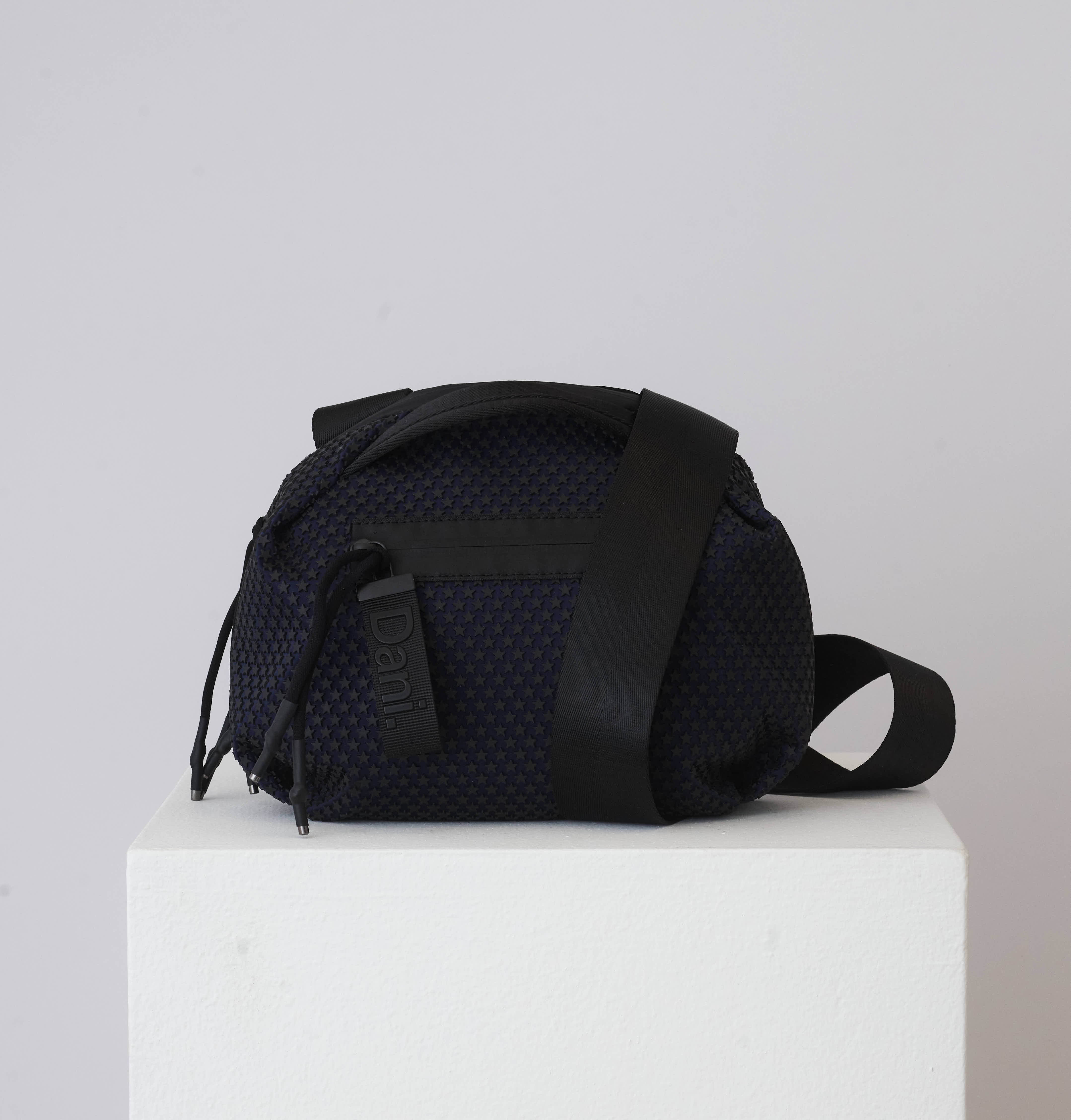 Black textured bag on a white pedestal with a light gray background
