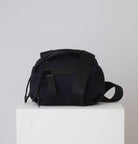 Black textured bag on a white pedestal with a light gray background