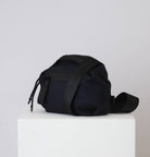 Black textured bag on a white pedestal with a light gray background