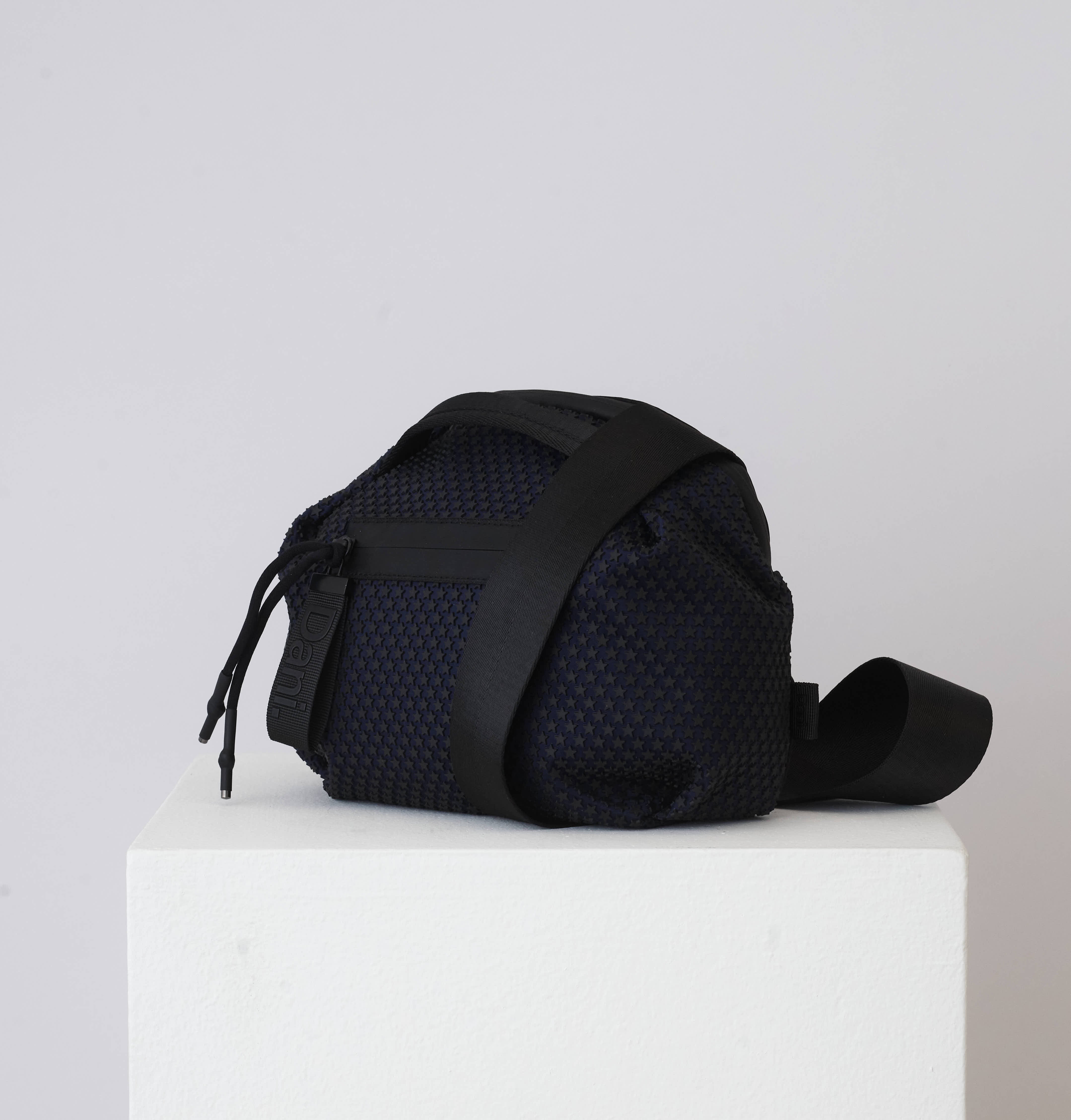 Black textured bag on a white pedestal with a light gray background