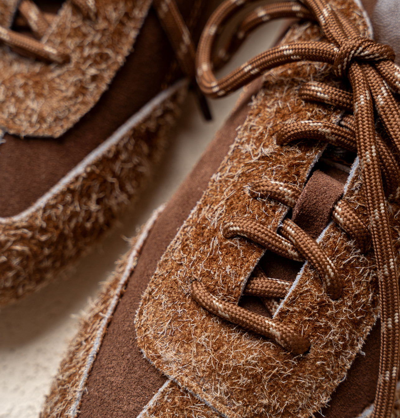 סניקרס חומות עם שרוכים, משלבות זמש ומרקם סיבים רופפים.