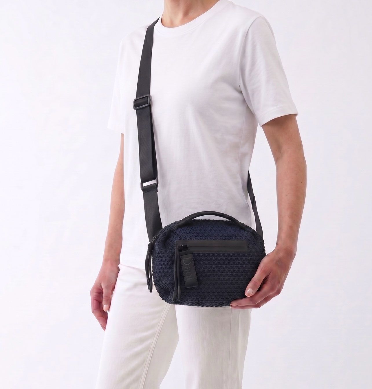 Person wearing a navy crossbody bag on a white background